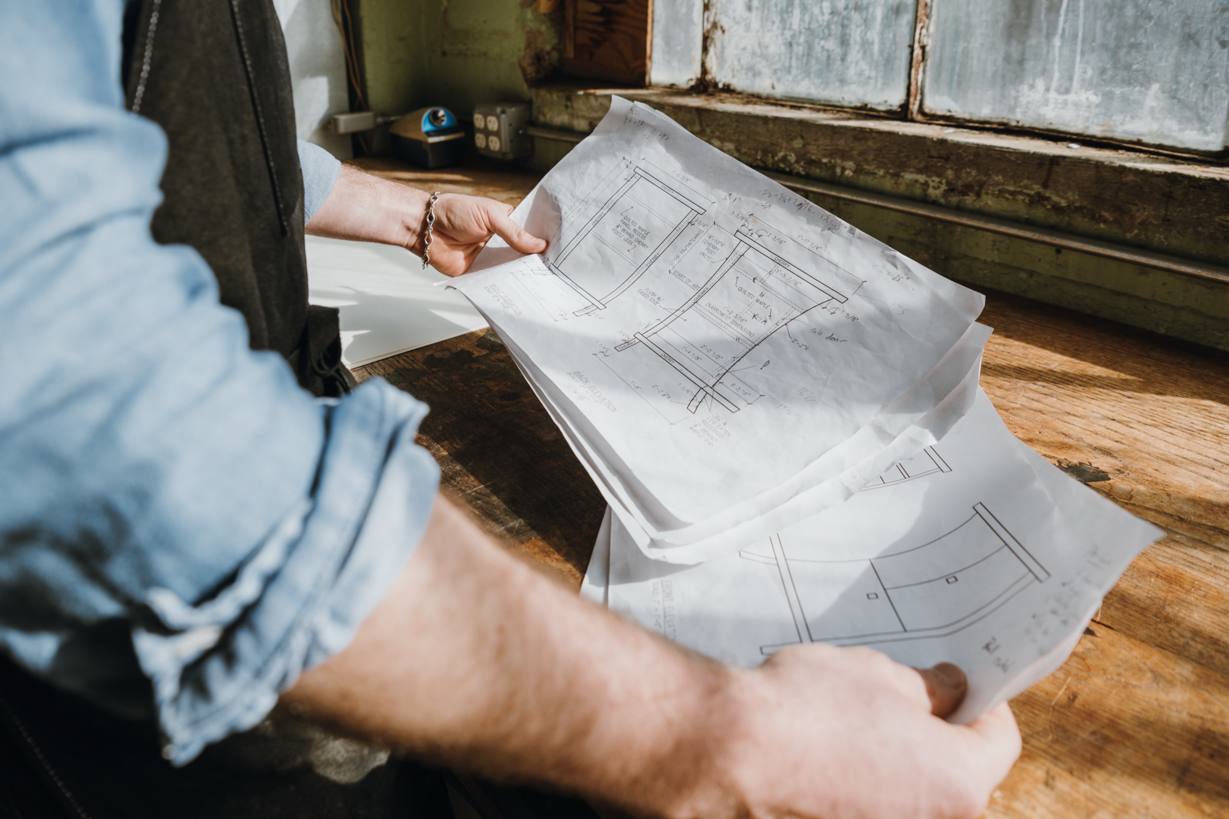 Reviewing hand-drawn nightstand design plans in the Flatow Furniture workshop