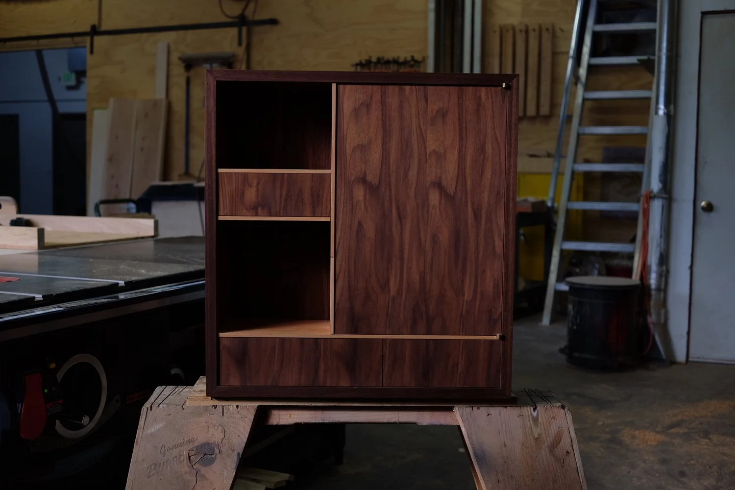 A walnut cabinet with open and closed compartments in a woodworking shop