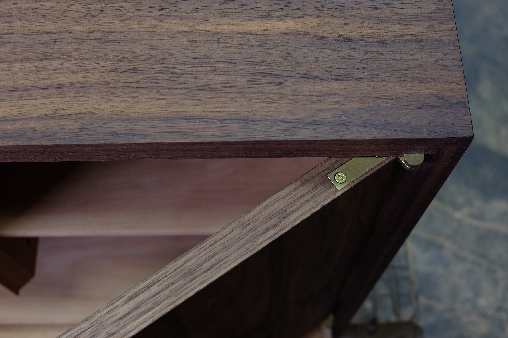 Close-up of walnut cabinet corner showing brass hinge detail