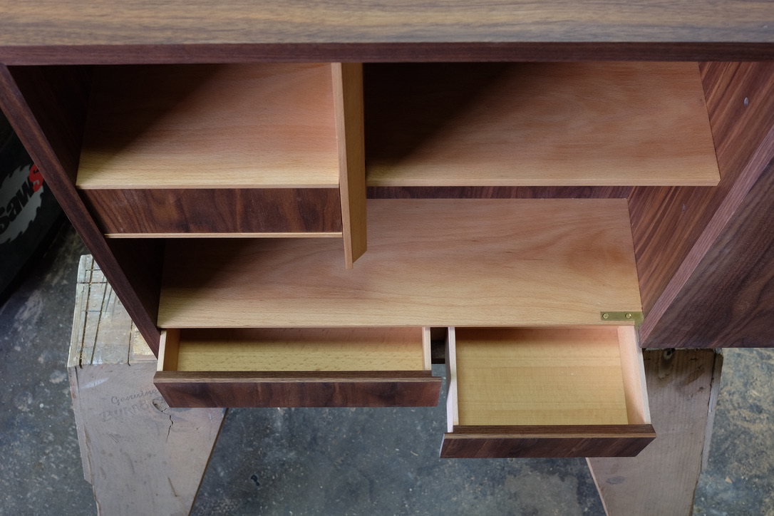 Top-down view of walnut cabinet interior showing compartments and brass hinges