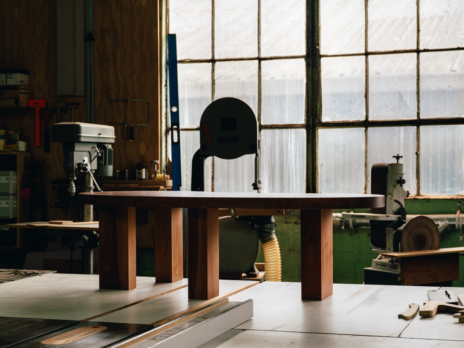 Madrone coffee table with chunky through-mortise legs silhouetted against workshop windows