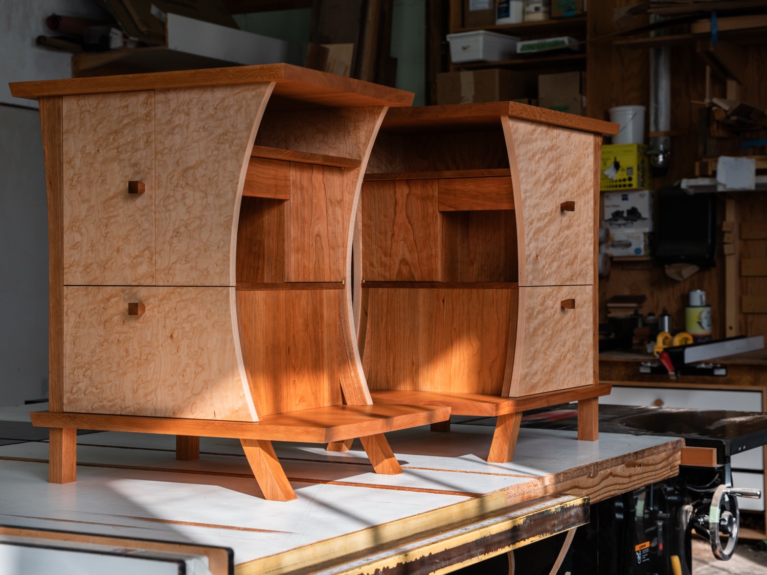 Pair of cherry and birdseye maple nightstands with curved sides and walnut pulls in workshop