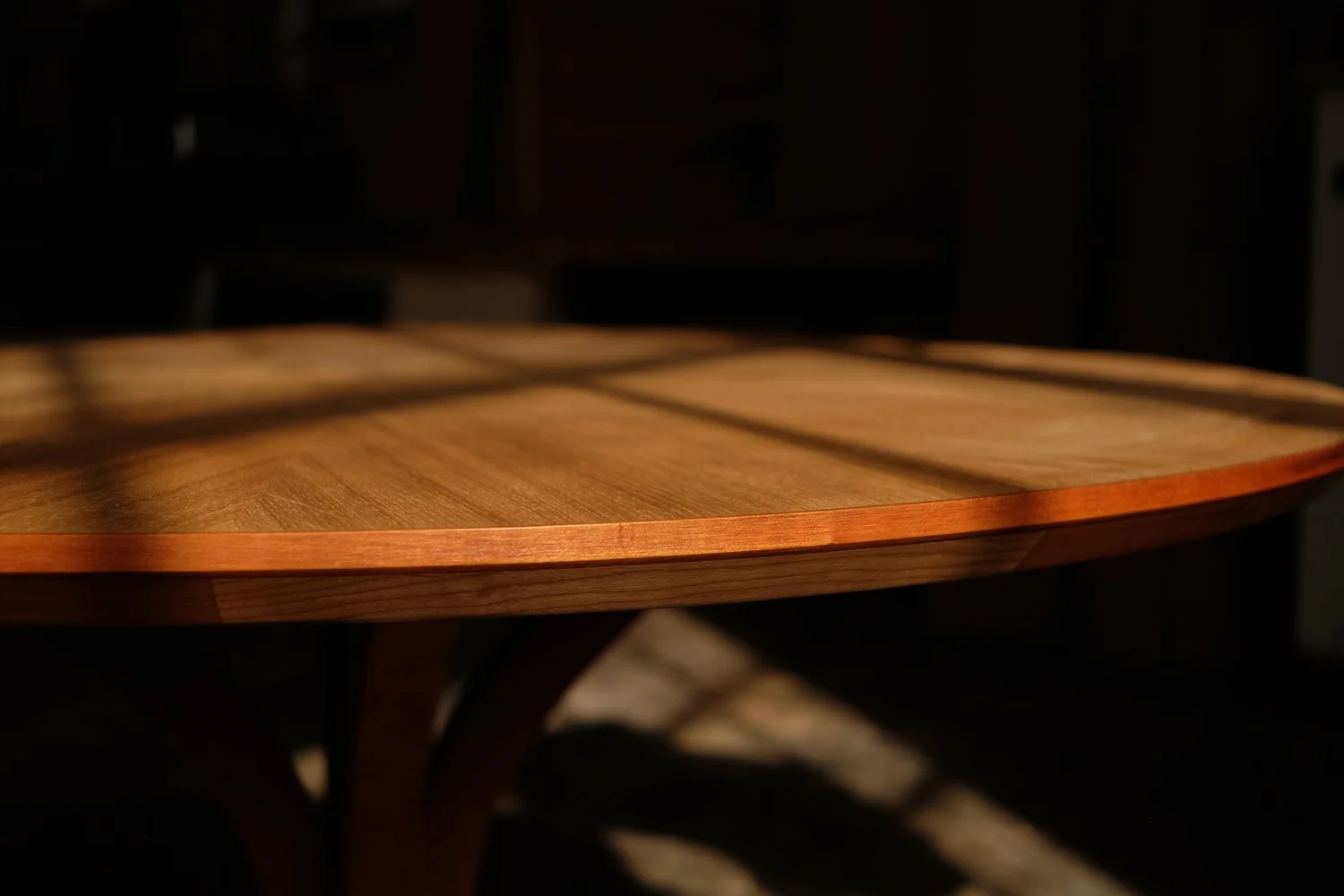 Close-up of a round white oak table with sunlight casting striped shadows across its surface