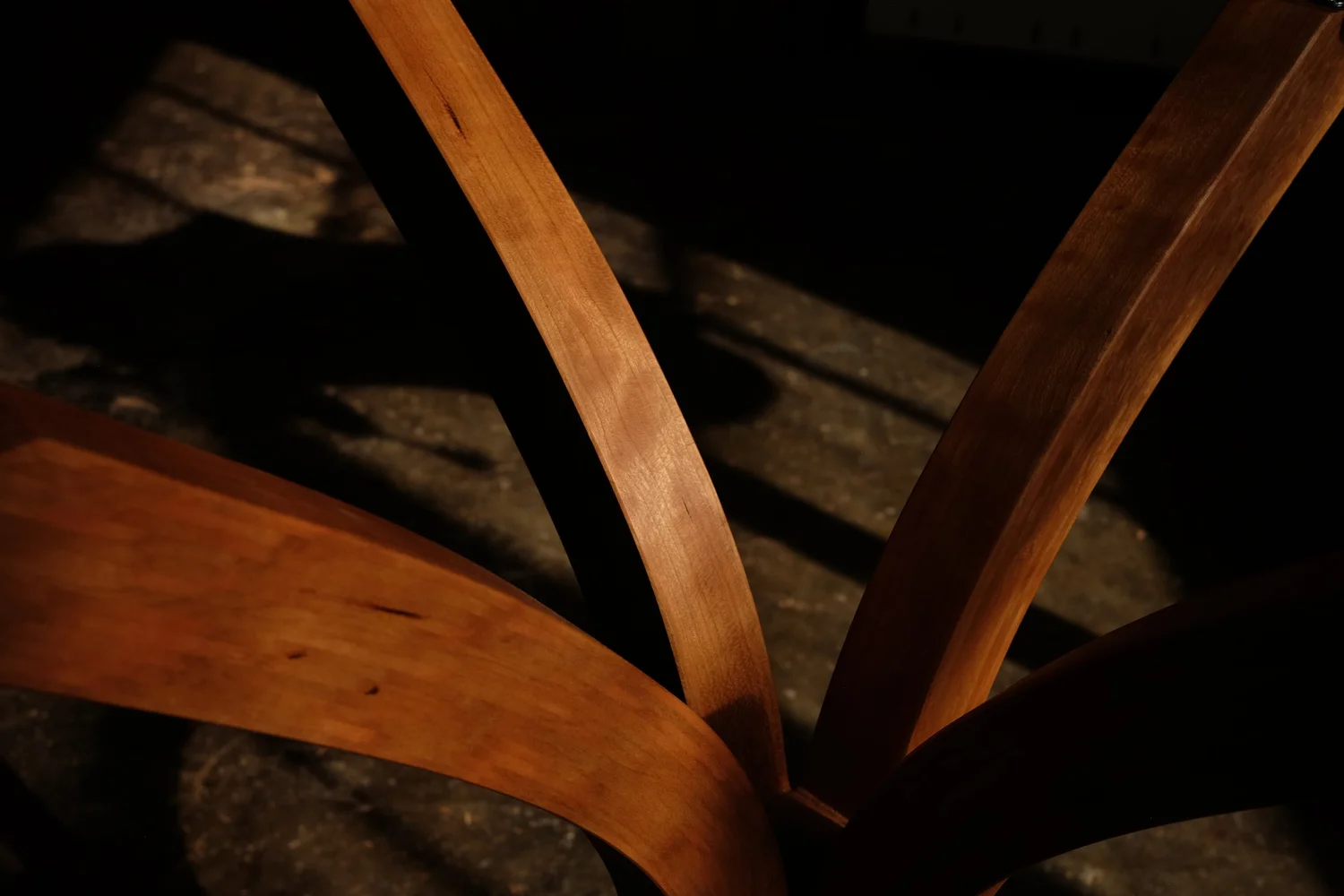 Close-up of curved table legs and part of the seat with shadow cast on a workshop floor