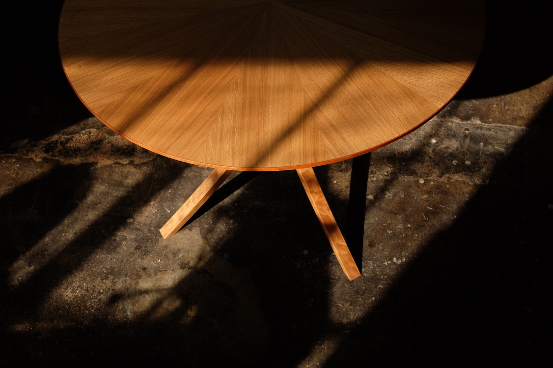 Overhead view of a round white oak dining table showing radial grain pattern with sunlight