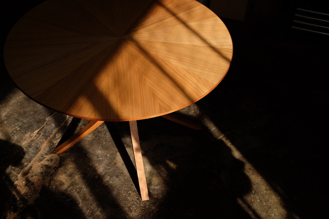 Angled overhead view of round white oak dining table showing sunburst grain and curved legs